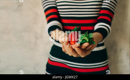Femme détient des fraises dans ses mains, robe rayée hors focus Banque D'Images