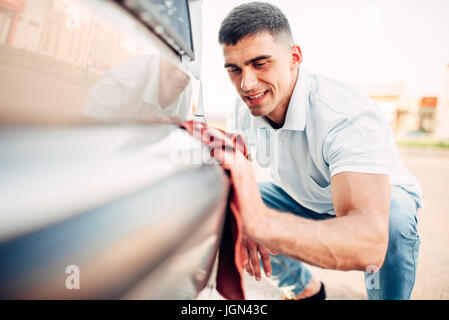 Polissage extérieur voiture sur la station de lavage. L'homme frotte pare-choc du véhicule automobile avec polish Banque D'Images