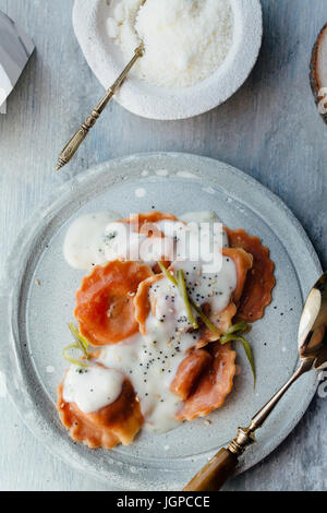 Carotte pâtes farcies de fromage et légumes, avec sauce béchamel, sur la plaque et sur fond bleu. Set. Banque D'Images