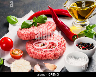 Vue rapprochée de la viande crue deux escalopes steak pour burger avec légumes, épices, basilic frais, huile d'olive. Faire des hamburger. Banque D'Images