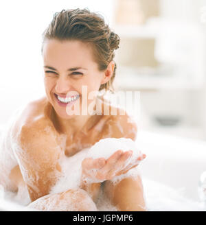 Portrait of happy young woman playing avec mousse dans la baignoire Banque D'Images