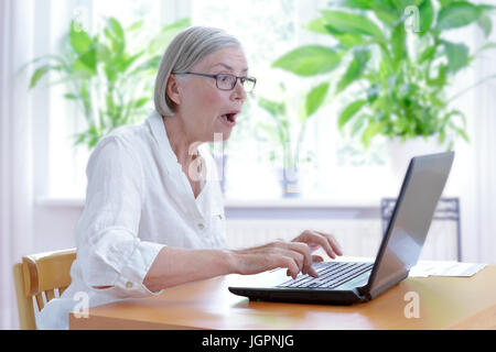 Femme senior à la maison dans son salon en regardant un choc à l'écran de son ordinateur portable, internet security concept Banque D'Images