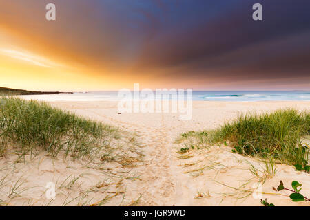 Des traces de pas dans le sable d'une plage de ronde mènent à une belle et spectaculaire lever du soleil sur la mer. Banque D'Images
