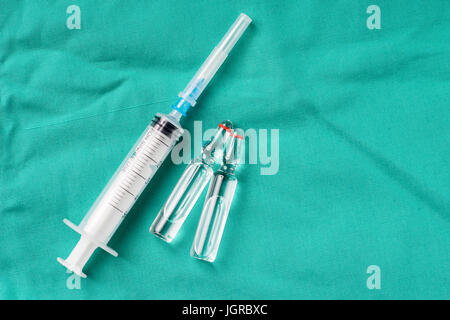 Flacons et seringues médicales allongé sur le fond vert de l'hôpital. L'arrière-plan peut être une partie du textile un médecin ou infirmière uniforme de travail. Banque D'Images