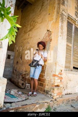 MADAGASCAR, Diego Suarez - décembre 3, 2014 : La fille avec le téléphone mobile se trouve près de la maison sur la rue. Madagascar, Diego Suarez. Banque D'Images