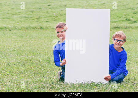 Garçon assis sur l'herbe avec étiquette blanche verticale à l'extérieur du conseil Banque D'Images