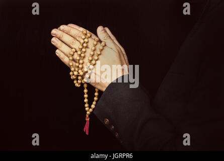 Hands holding rosary et plié dans la prière sur un fond noir. Banque D'Images