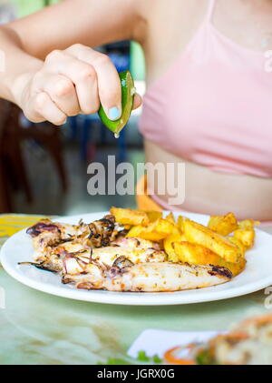 La main féminine squeezing lime sur Calmar grillé avec frites Banque D'Images