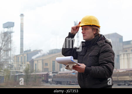 Sugar Refinery worker standing outdoors , portant un casque de protection et des presse-papiers jaune tenant dans ses mains. Banque D'Images