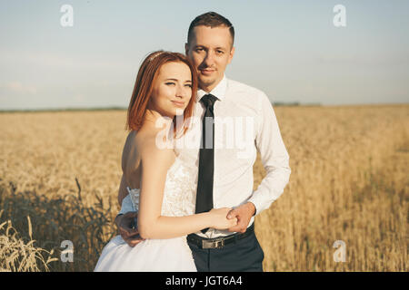 Magnifique mariée et le marié en champ de blé. Le bonheur et le mariage. Femme en robe blanche homme en chemise blanche et cravate serrant les uns les autres. Banque D'Images