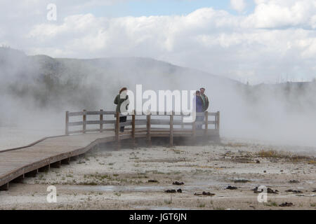 Trois personnes sont debout sur la promenade à la vapeur produite par Piscine Arc-en-ciel dans le bassin de sable noir, Upper Geyser Basin, Parc National de Yellowstone Banque D'Images