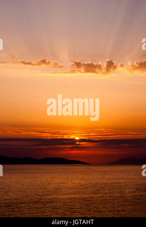 Vertical image de coucher de soleil doré avec faible au niveau central au-dessus de la mer et du soleil qui traverse des nuages au-dessus, avec du soleil dans le centre de l'image Banque D'Images