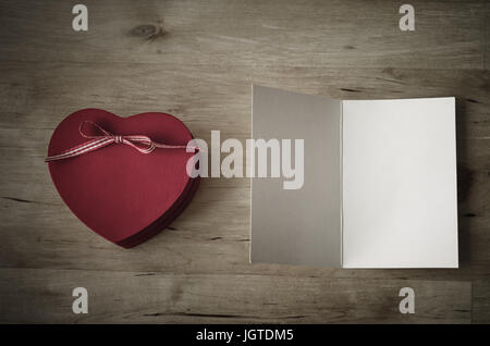 Passage tiré d'un rouge en forme de coeur en bois peint boîte-cadeau avec ruban bow, et une carte de vœux, laissée en blanc pour un message.effet vintage avec Banque D'Images