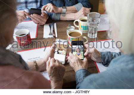 Les femmes âgées amis échangeant des photos numériques, des petits-enfants sur les téléphones avec appareil photo in diner