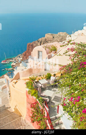 Young caucasian man sitting at table sur belle terrasse de café avec des fleurs à l'heure du déjeuner à la recherche en mer aux beaux jours d'été à Oia, Santorini Banque D'Images