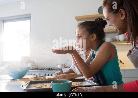 Mère et fille soufflant la farine dans la cuisine à la maison Banque D'Images