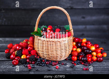 Mélange de petits fruits dans le panier sur fond de bois foncé Banque D'Images