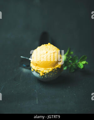 Cuillère à crème glacée de sorbet mangue dans la crème glacée sur une pelle en bois noir background, close-up. Manger propre, sain, végétarien, perte de poids, de mourir Banque D'Images