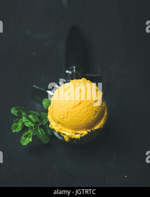 Cuillère à crème glacée de sorbet mangue dans une pelle de la crème glacée à la menthe fraîche sur fond de bois noir. Manger propre, sain, végétarien, perte de poids, l'alcali Banque D'Images