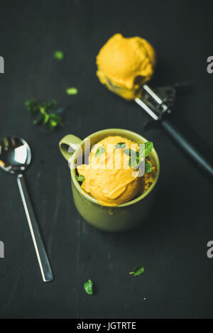 Dessert d'été rafraîchissante. Sorbet mangue boules de glace avec des feuilles de menthe fraîche dans le bol vert sur fond de bois noir. Manger sain, propre, weig Banque D'Images