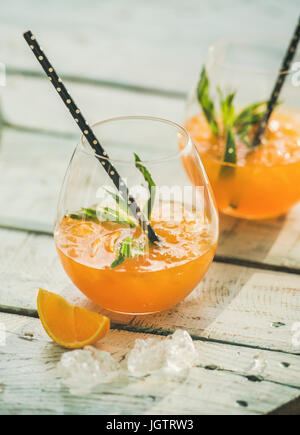 Boissons froides rafraîchissantes cocktail d'été avec orange, menthe et de la glace de verres sur table en bois bleu clair, fond selectiv Banque D'Images