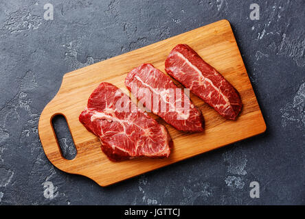 La viande fraîche crue lame supérieure steaks sur une planche à découper en bois sur fond sombre Banque D'Images