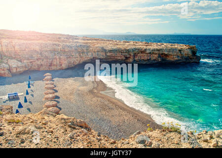 L'image traitée de petite plage avec aucun peuple au lever du soleil avec des parasols et des chaises longues entre deux falaises de Skaleta, Crète, Grèce Banque D'Images
