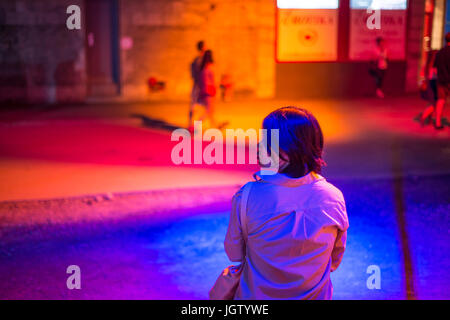 Vue arrière d'un young asian woman sitting on the Street la nuit pendant le festival Montréal Banque D'Images