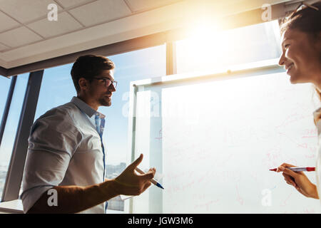 Collègues de bureau discuter affaires Idées en salle du Conseil. L'homme et la femme la rédaction de notes office contre soleil éclatant en arrière-plan. Banque D'Images