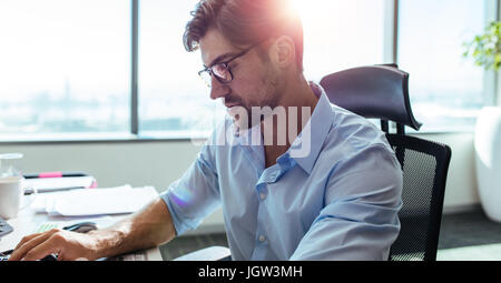 Gros plan du businessman assis à son bureau en bureau. Homme portant lunettes, assis à son poste de travail à la recherche vers le bas à son bureau. Banque D'Images