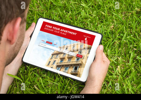 Jeune homme de visiter un appartement en location site web avec tablette et regarder l'écran, allongés sur l'herbe. Banque D'Images