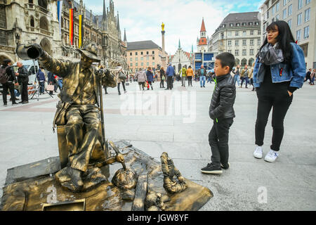 MUNICH, ALLEMAGNE - le 9 mai 2017 : un jeune garçon et d'une mère regardant un artiste de rue déguisés en une sculpture fontaine avec des personnes dans l'arrière-plan sightse Banque D'Images