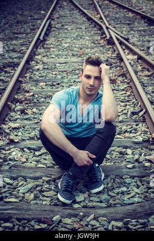 Young man sitting on railroad Banque D'Images