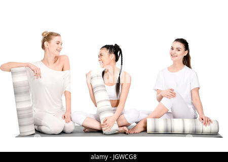 Smiling girls multiethnique se reposant après la formation de yoga et d'un salon avec un tapis de yoga isolated on white Banque D'Images