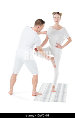 Attractive blonde woman practicing yoga pose d'arbres avec formateur isolated on white Banque D'Images