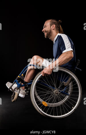 Heureux en fauteuil roulant paralympique habillé en sportswear isolated on black Banque D'Images