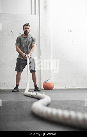 Homme travaillant sur la bataille avec la corde dans l'entraînement en salle de sport Banque D'Images