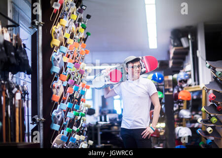 Jeune homme avec la planche à roulettes par-dessus son épaule en skateboard shop Banque D'Images