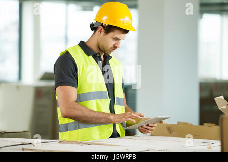 Homme portant un gilet haute visibilité, debout dans l'espace nouvellement construit, looking at digital tablet Banque D'Images