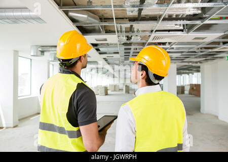 Deux hommes portant le gilet haute visibilité, having discussion dans la construction de l'espace de bureau, vue arrière Banque D'Images