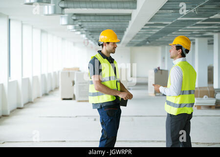 Deux hommes portant le gilet haute visibilité, having discussion dans la construction de l'espace de bureau Banque D'Images