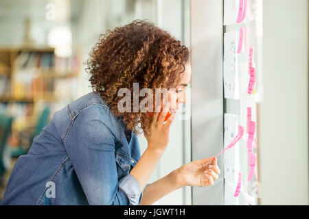 Digital designer féminin faisant appel à la recherche et à l'office de mur Banque D'Images