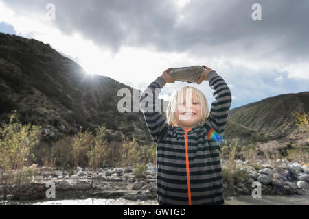 Portrait of cute boy holding up rock à partir de la rivière Banque D'Images