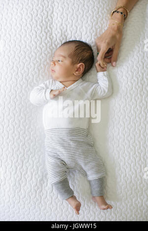 Baby Boy lying on bed, mother holding baby's hand, overhead view Banque D'Images