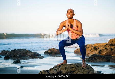 Jeune femme debout sur les rochers, sur la plage, accroupie, les mains Banque D'Images