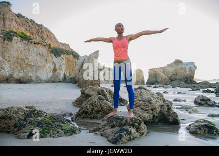 Jeune femme debout sur des rochers sur la plage, les bras tendus