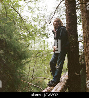 Portrait de garçon, debout sur log, leaning against tree Banque D'Images