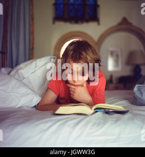 Boy relaxing on bed, reading book Banque D'Images