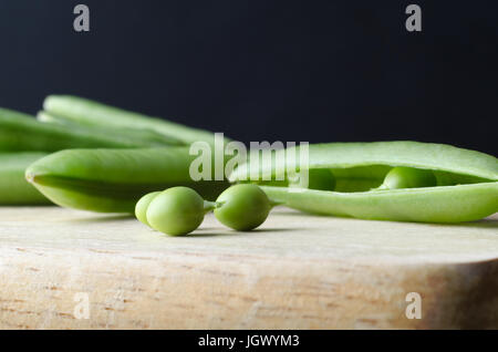 Gros plan (macro) de trois tiges de pois avec intacte sur la planche à découper en bois. Le pod ouvert dont il est extrait est à l'origine, et non ouvert po Banque D'Images