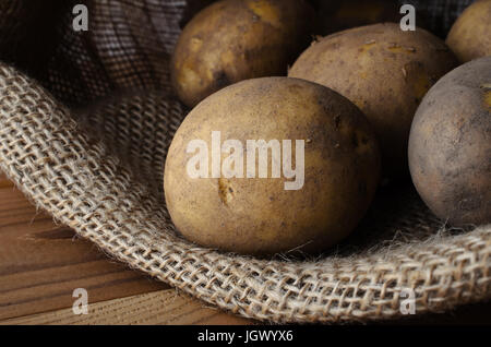 Les matières, les laver, les pommes de terre non pelées dans ouvert sac en toile de jute, lain sur bois revêtus de table. Banque D'Images